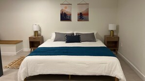 A bedroom with a bed, two nightstands, a wall-mounted lamp, and two framed pictures.