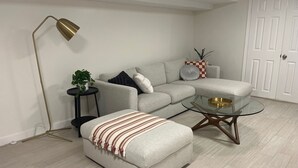 A modern living room with a grey sofa, a glass coffee table, a floor lamp, and a small side table with a plant.