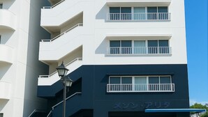 Ein modernes Mehrfamilienhaus mit Balkonen und einem Schild mit der Aufschrift 'メゾン・アリタ'.