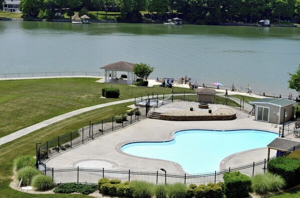 A swimming pool with a surrounding fence, a gazebo, and a small pavilion by the water.