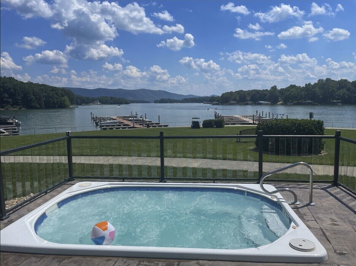 Ett bubbelbad med utsikt över en sjö och båtar, omgivet av en terrass med ett räcke.