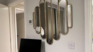 A white desk with a laptop, a black monitor, and a wall-mounted mirror. - Double room in Luxury new flat. 1min to bus stop & grocery store! (Brentford)