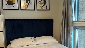 A neatly made bed with a dark headboard, a set of towels, and three abstract art pieces on the wall. - Double room in Luxury new flat. 1min to bus stop & grocery store! (Brentford)