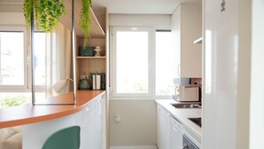 Cocina compacta con armarios blancos, encimera de madera y ventana que aporta luz natural.