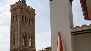 Un balcón con vistas a una torre histórica, una sombrilla moderna y un suelo de baldosas.