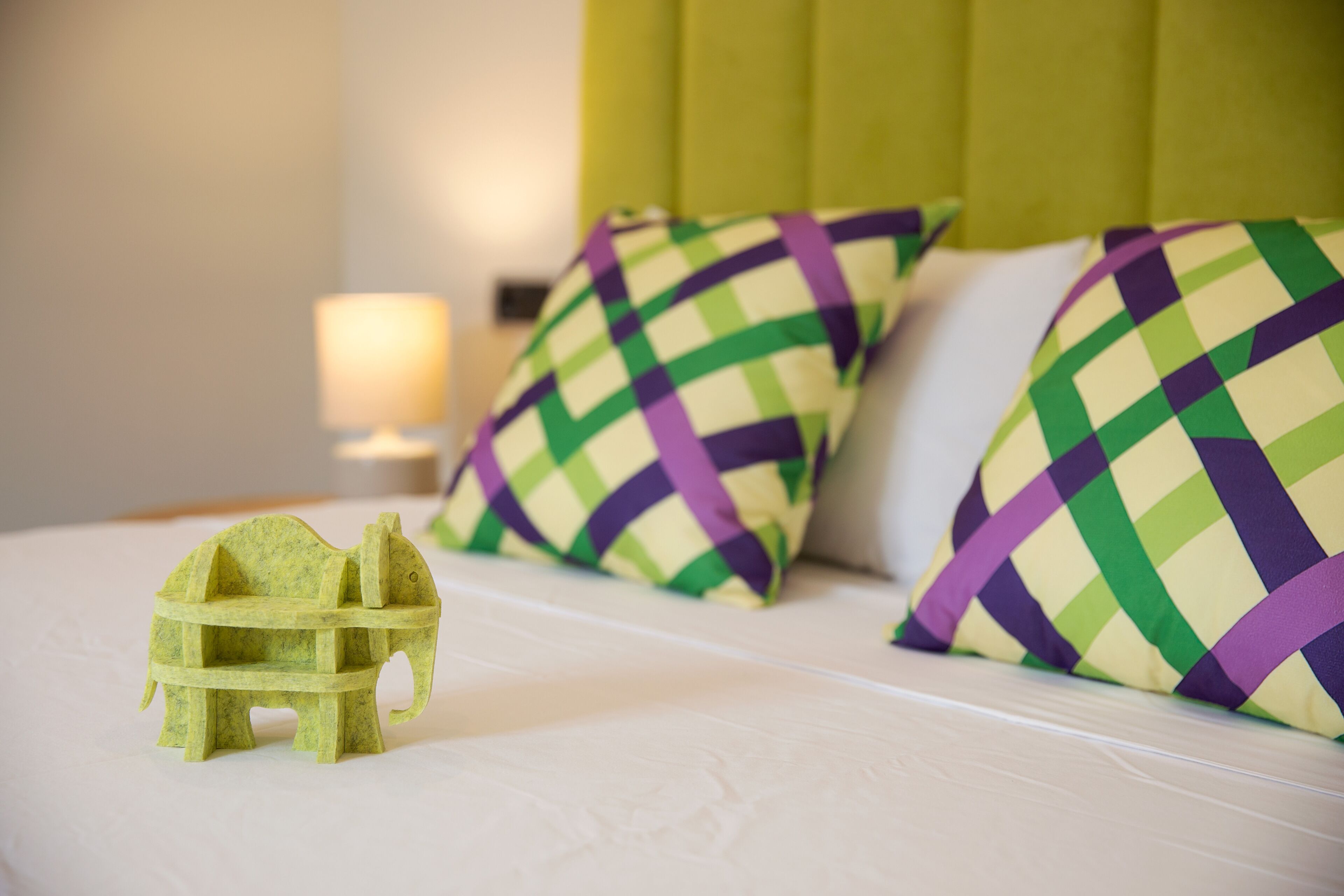A bed with a green and purple checkered pillow, a small green elephant-shaped object, and a green headboard.