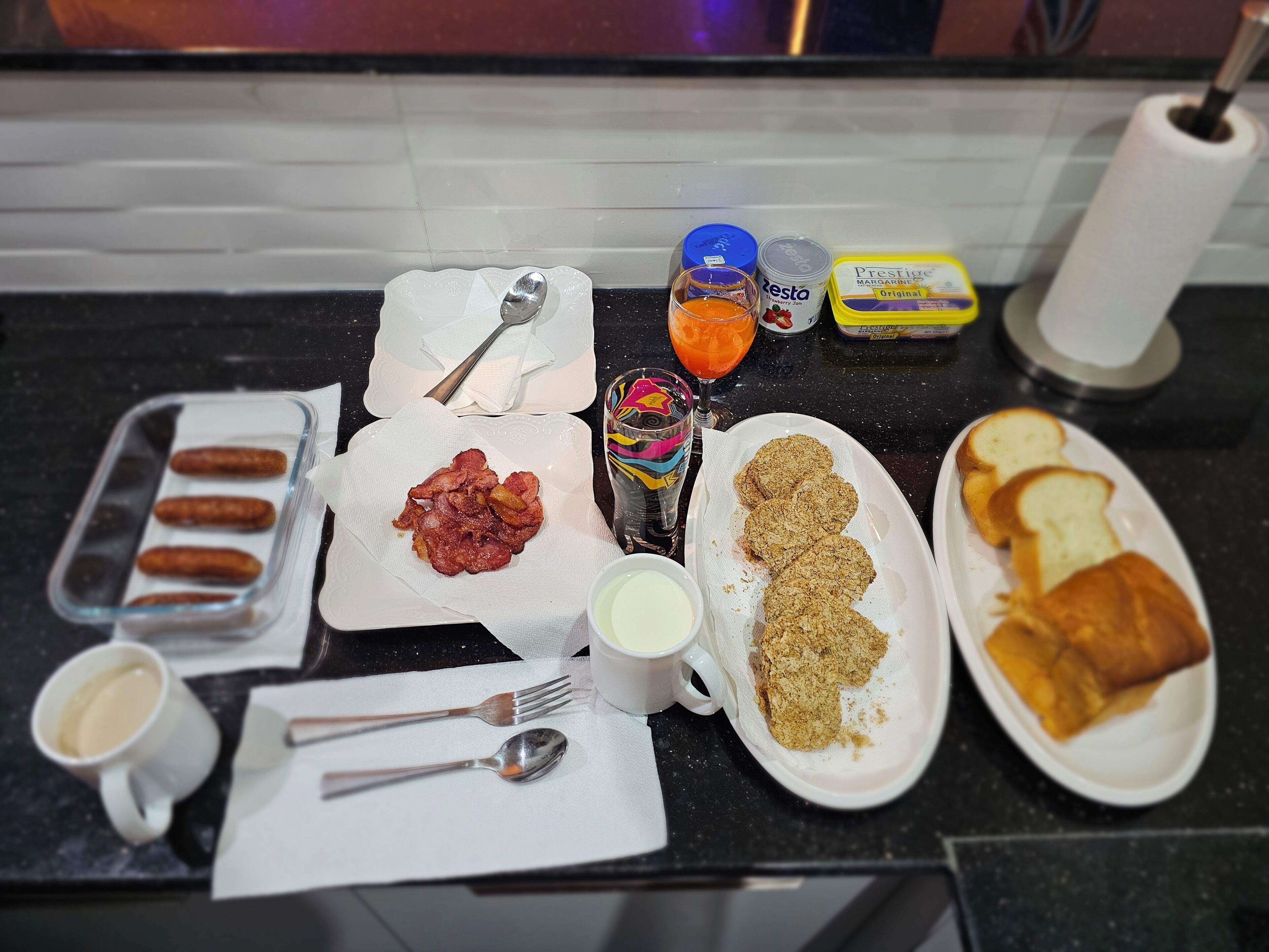 A breakfast table with various food items and utensils.
