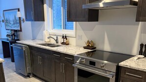Una cocina moderna con armarios oscuros, estufa de acero inoxidable y una ventana sobre el lavamanos.