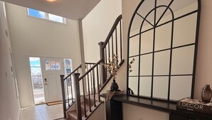 Un interior moderno con una escalera de madera, una consola negra y un amplio ventanal arqueado.