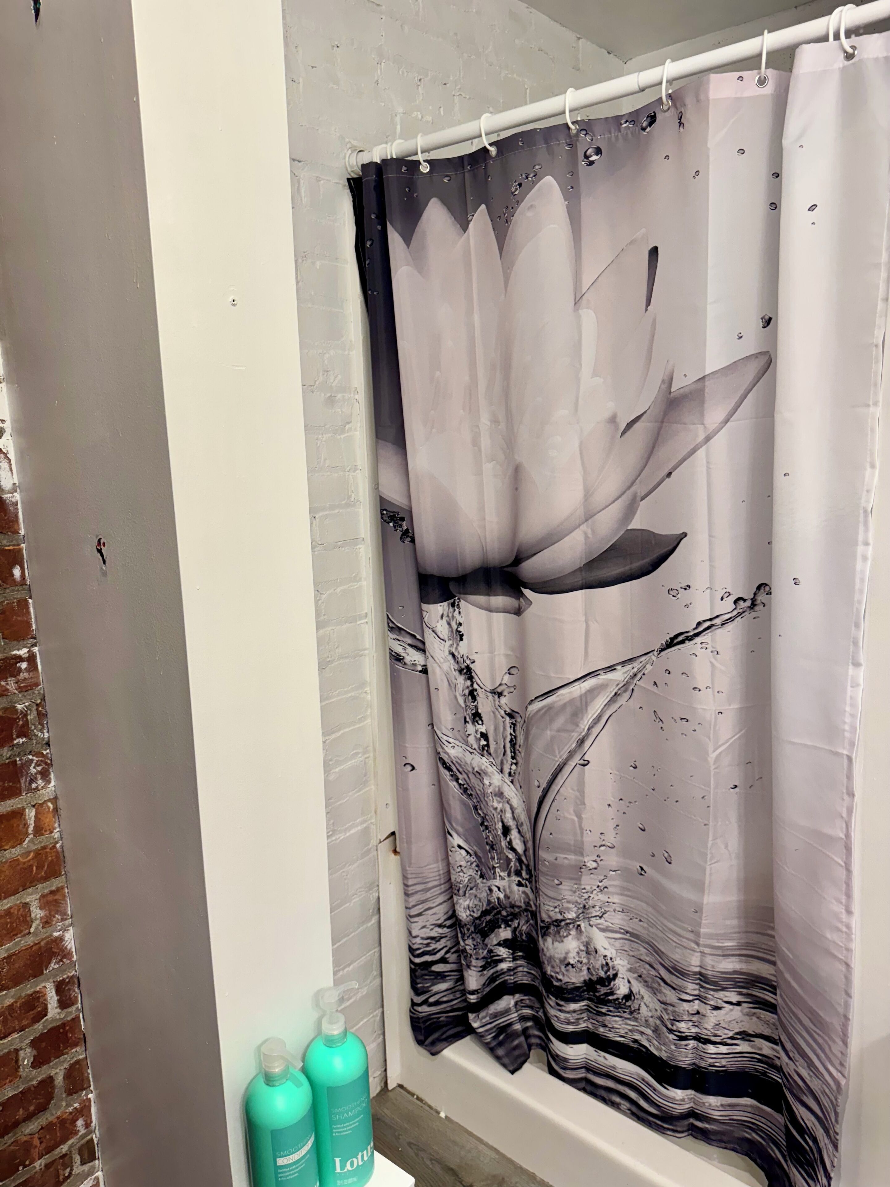 A bathroom with a shower curtain featuring a lotus flower design, a white bathtub, and two bottles of lotion on the floor.