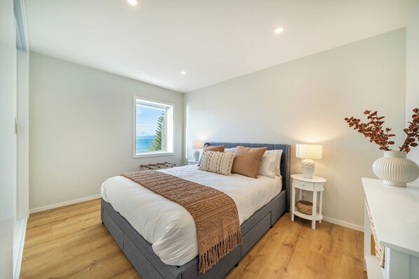 A bedroom with a large bed, a nightstand, a lamp, and a view of the outdoors.
