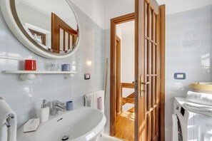 A modern bathroom with a white sink, mirror, and wooden door leading to a laundry area. - La Casa Di Dadà with Terrace and Garden, Oulx, Italy (Oulx)
