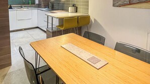 A modern kitchen with white cabinets, a wooden dining table, and a pendant light. - Entire Birmingham Home | Sleeps 4, Parking & Garden (Lozells)