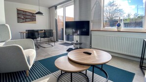 A modern living room with a TV, two round tables, a sofa, and a dining area with chairs. - Entire Birmingham Home | Sleeps 4, Parking & Garden (Lozells)