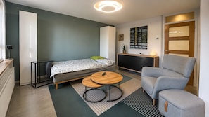 A compact room with a bed, a sofa, a small table, and a fireplace.