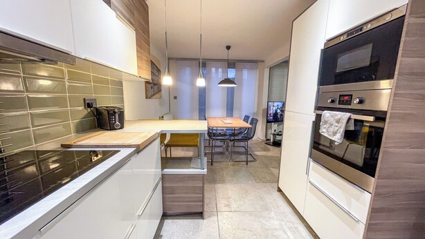 A modern kitchen with a built-in oven, a toaster, and a dining area with a table and chairs. - Entire Birmingham Home | Sleeps 4, Parking & Garden (Lozells)