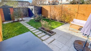A backyard with a patio area, a wooden fence, and a small garden. - Entire Birmingham Home | Sleeps 4, Parking & Garden (Lozells)