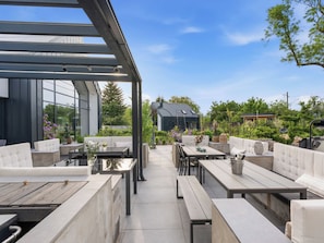 An outdoor patio with modern furniture, a glass enclosure, and a view of a house and garden.