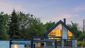 Een modern huis met een groot raam, een vijver met groene verlichting en een houten terras.