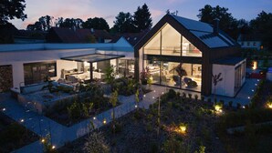 Een modern huis met een grote glazen gevel, een overdekt terras en een verzorgde tuin.