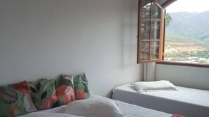 A hotel room with two beds, a red blanket, and a window with a view of a mountainous landscape. - Mumu's Corner (Ouro Preto)