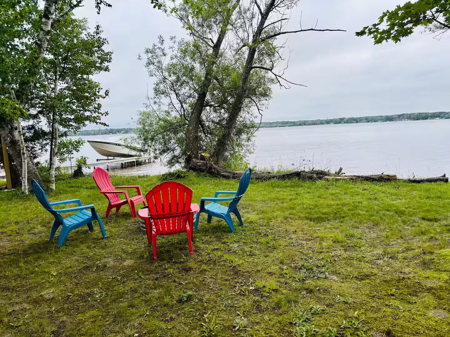 A lakeside setting with a grassy area, a red chair, and two blue chairs.