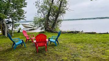 A lakeside setting with a grassy area, a red chair, and two blue chairs.