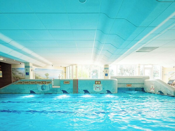 Una piscina interior con agua cristalina, paredes de azulejos y un techo de diseño ondulado.