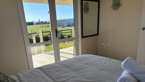 A bedroom with a bed, a view of a green field, and a door leading to an outdoor area.