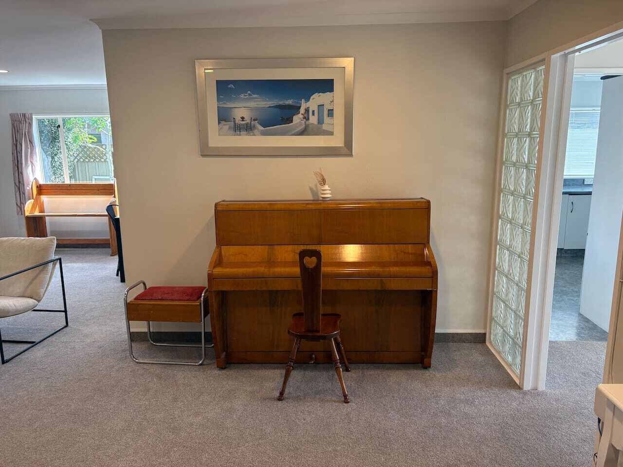 Een kamer met een houten piano, een stoel, een tafeltje en een lijst met een foto aan de muur.