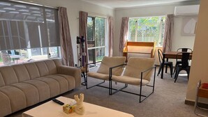 Ein modernes Wohnzimmer mit Sofa, Couchtisch und Sessel. Im Hintergrund steht ein Esstisch mit Stühlen.