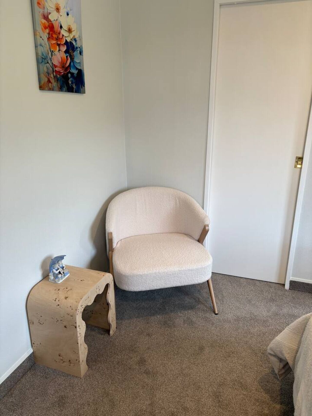 Ein Zimmer mit einem beigefarbenen Sessel, einem kleinen Holzschemel und einem Bild an der Wand.