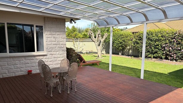 Eine überdachte Terrasse mit Tisch und Stühlen, eine Ziegelwand und Blick auf einen Garten.