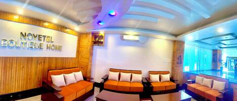 Eine Hotelhalle mit Holzwand, orangefarbenen Sofas und einem Schild mit der Aufschrift "NOVETEL BOUTIQUE HOME".