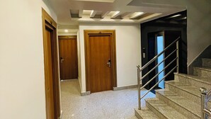 Un pasillo con suelo de mármol, puertas de madera y una escalera con barandillas de metal.