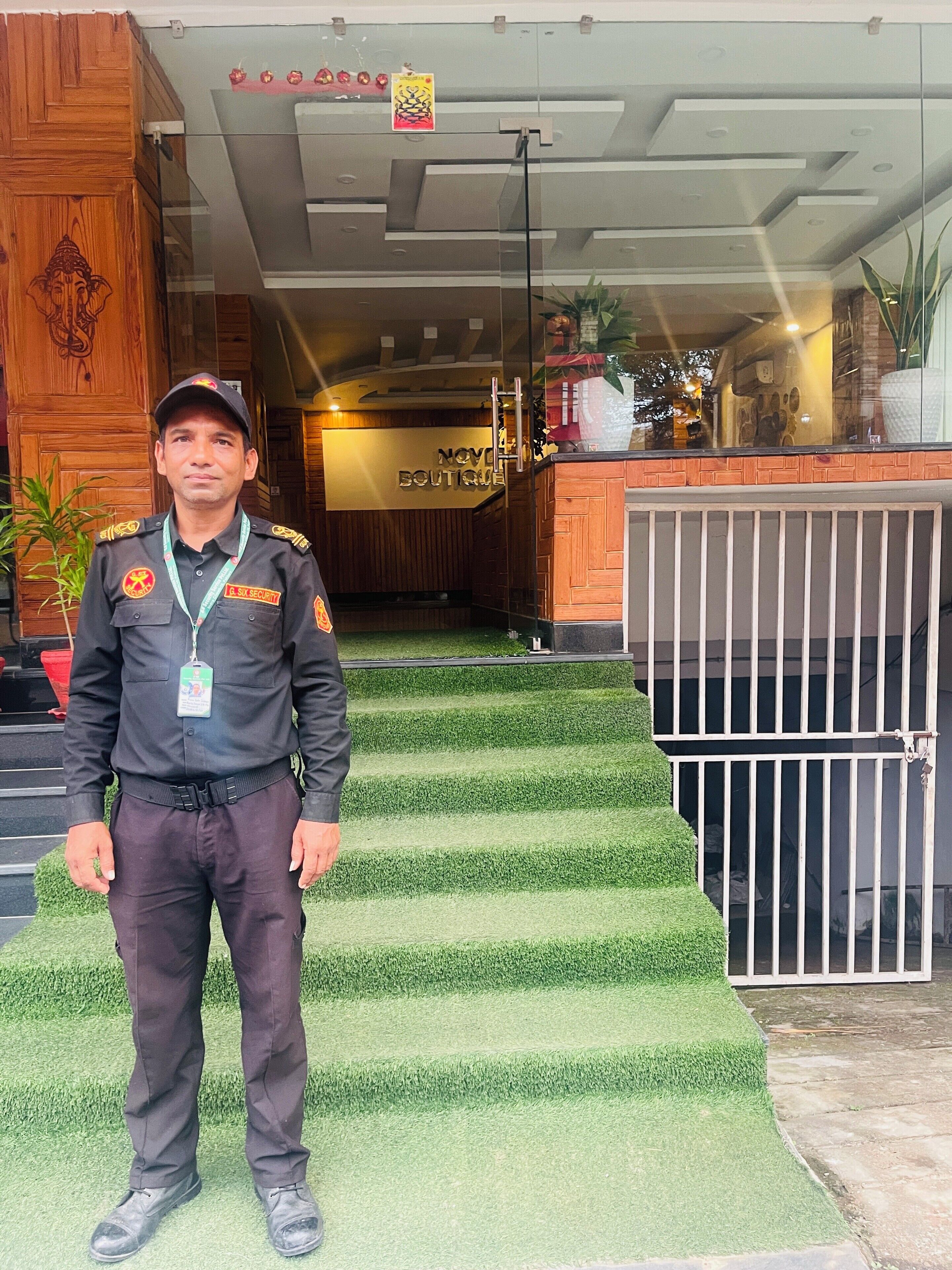 A security guard standing in front of a boutique hotel entrance with a wooden facade, a signboard, and a staircase leading to the entrance.