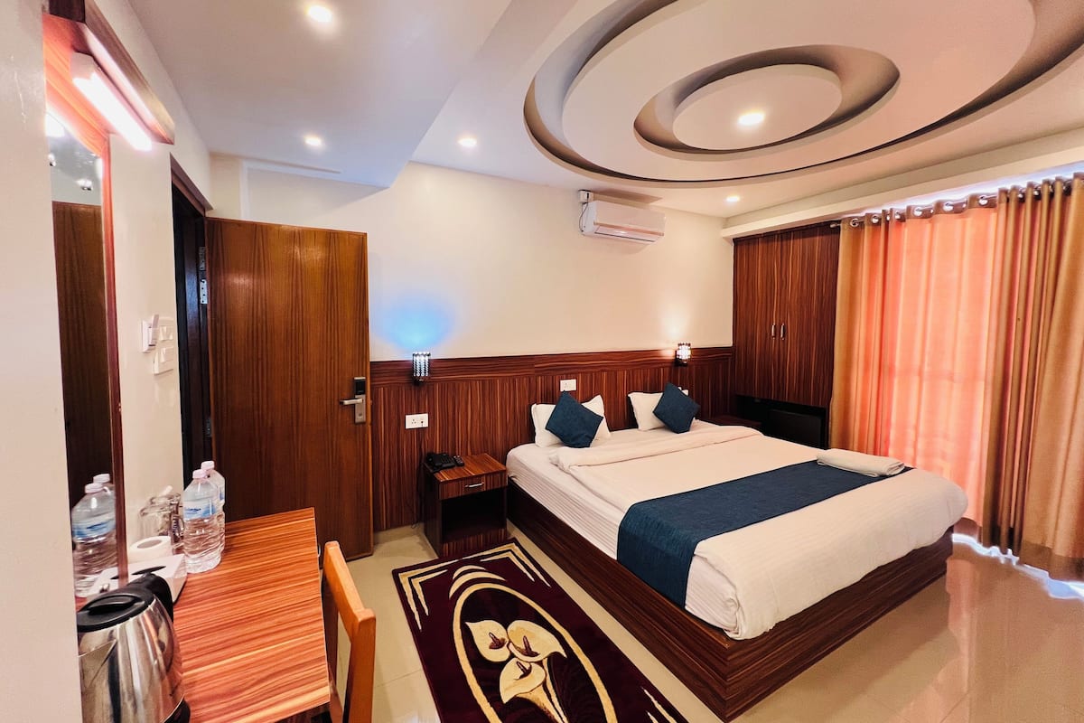 A hotel room with a bed, a desk, a chair, a kettle, and a water dispenser.