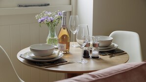 Una mesa de comedor con cuencos blancos, una botella de vino rosado espumoso, copas de vino y un florero con flores.