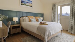 Un dormitorio ordenado con cama, mesitas de noche, una silla y una ventana con cortinas.