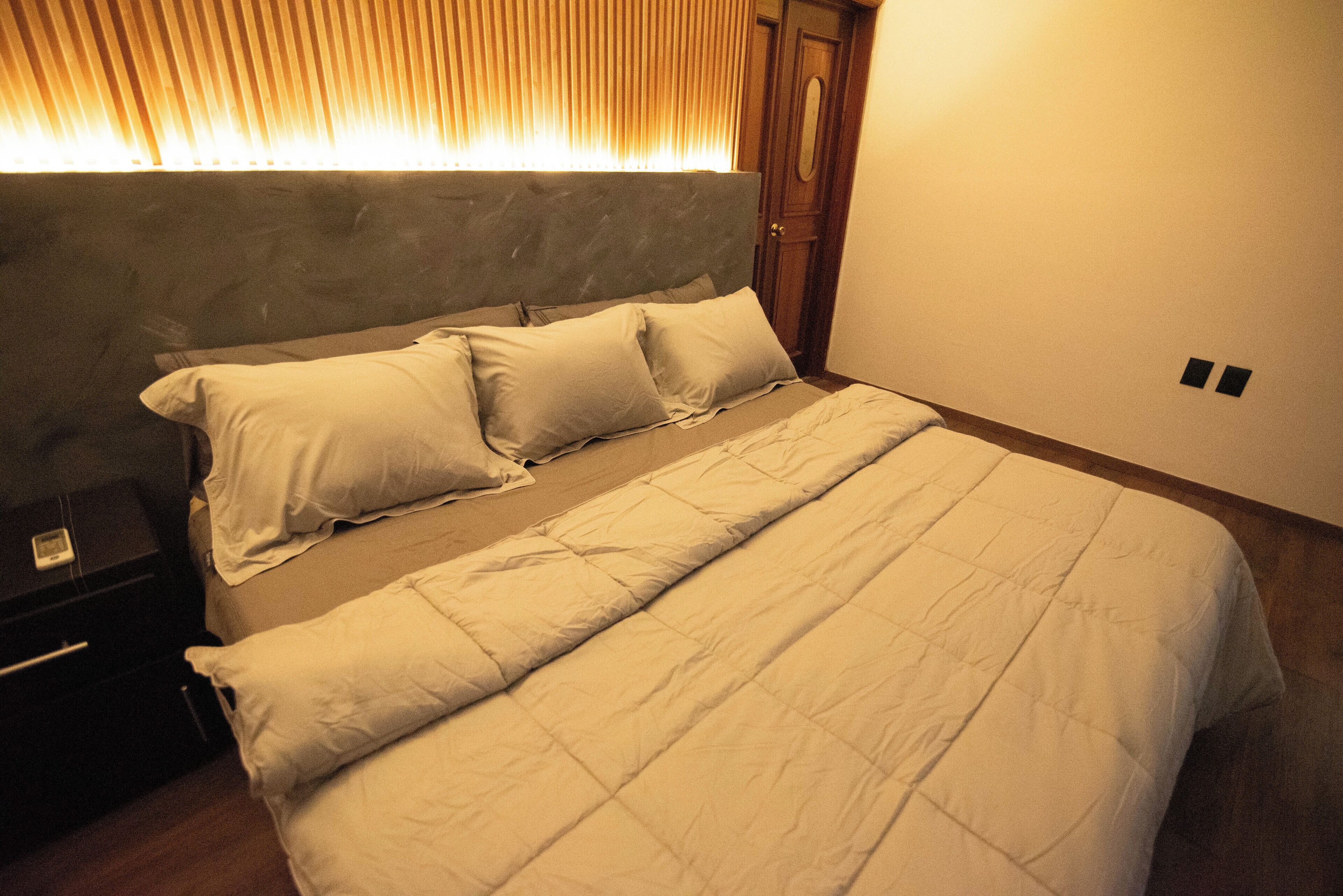 A neatly made bed with a grey headboard and white bedding in a room with wooden flooring and a wooden door.