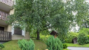 Ein Wohngebäude mit Balkon, umgeben von üppiger Vegetation und einer kleinen Holzkonstruktion.