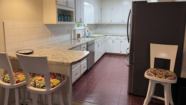 A kitchen with white cabinets, a granite countertop, a refrigerator, and two stools with floral cushions. - Charming, newly renovated 3-bedroom house just minutes from downtown Oxford. (Oxford)
