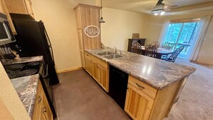 A kitchen with wooden cabinets, a granite countertop, a black dishwasher, and a 'Blessed' sign. - Gold Pan Hideaway (Hill City)