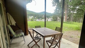 A covered patio with a table and chairs, overlooking a green landscape with hills. - Gold Pan Hideaway (Hill City)