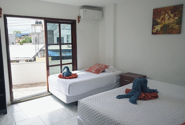A hotel room with two beds, a sliding glass door to the outside, and a painting on the wall. - Carpao Lodge (Puerto Ayora)