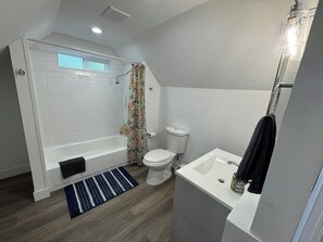Een badkamer met douche, toilet, wastafel en een raam.