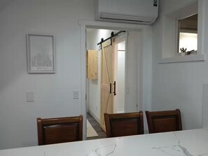 Een eetruimte met een marmeren tafel en houten stoelen, een ingelijste foto aan de muur, en een schuifdeur die leidt naar een andere kamer.