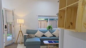 Ein gemütliches Wohnzimmer mit einem Ecksofa, einer Lampe, einem kleinen Tisch und Blick ins Freie.