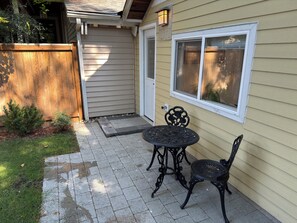 Een terras met een tafel en stoelen, een houten omheining en een huis met beplating en een raam.