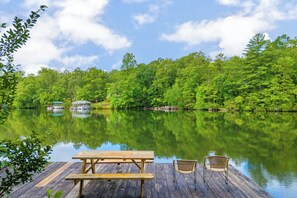 Une jetée en bois, avec une table de pique-nique et deux chaises, donnant sur un lac paisible, bordé d’une forêt dense et verdoyante.